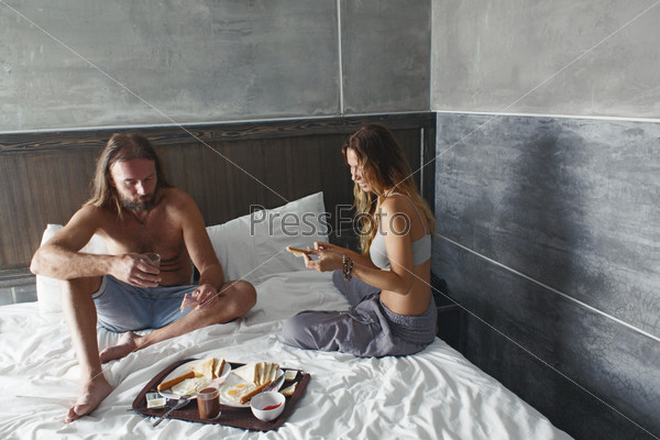 Couple having breakfast on a bed in luxury hotel with modern concrete design interior