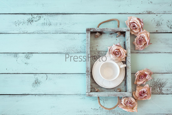 Vintage wooden tray with porcelain teacup and rose buds on shabby chic mint background, top view point