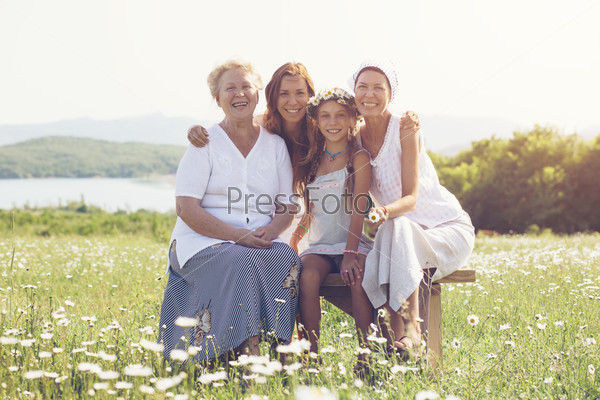 Four generations of beautiful women sitting together in a camomile field and smiling