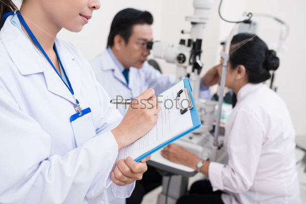 Assistant filling medical record while optometrist examining patient