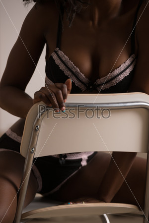 Beautiful alluring african woman in sexy lingerie. Portrait of beautiful sexy stylish young woman model with perfect clean skin in black lingerie posing on chair