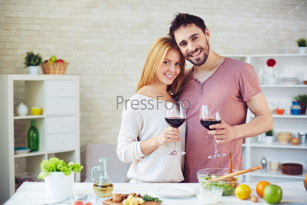 Young man and woman with red wine looking at camera in the kitchen