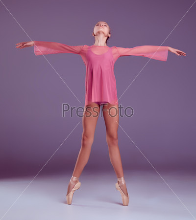 Young ballerina dancer in pink dress showing her techniques on lilac background