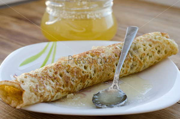 Rolled pancake  and honey on a wooden surface