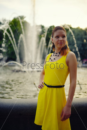 Portrait of the beautiful woman in yellow dress against the fountain