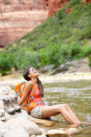 Relaxing hiker woman resting feet in river happy serene and relaxed afterhiking in Zion National Park. Female hiker in Zion Canyon wearing backpack. Healthy lifestyle multiracial Asian girl, Utah, USA