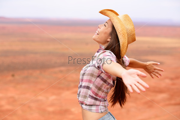 Cowgirl - woman happy and free on american prairie wearing cowboy hat with arms outstretched in freedom concept. Beautiful smiling multiracial Caucasian Asian young woman outdoors, Arizona Utah, USA.