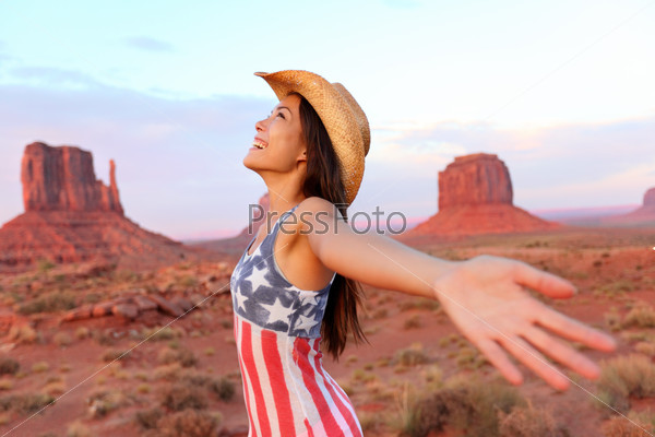 Cowgirl - woman happy and free in Monument Valley wearing cowboy hat with arms outstretched in freedom concept. Beautiful smiling multiracial young woman outdoors, Arizona Utah, USA.