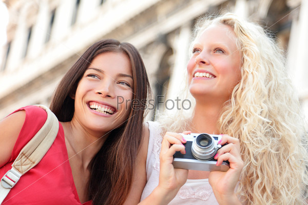 Girlfriends laughing having fun with camera taking picture with camera happy outside. Multiracial friends, Asian woman and Caucasian blonde traveling on San Marco Square, Venice, Italy