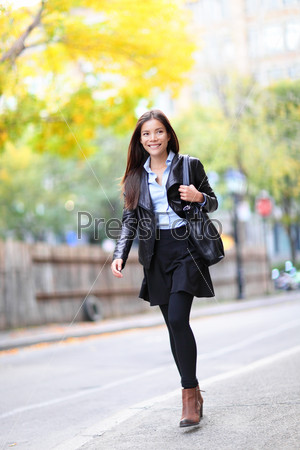 Young urban professional woman in walking in city. Fashion girl living city lifestyle in leather jacket in autumn fall. Trendy modern female. Multiracial Asian Caucasian model.