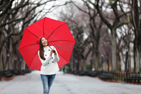 Woman with red umbrella walking in park in fall. Happy smiling multiracial girl walking cheerful with red umbrella in Central Park, Manhattan, New York City, USA.