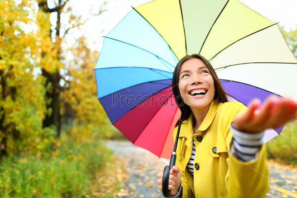 Autumn / fall woman happy in rain with umbrella. Female model looking up at clearing sky joyful on rainy fall day wearing yellow raincoat outside in nature forest by lake. Multi-ethnic Asian girl.
