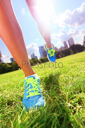 Runner - running shoes closeup of woman athlete running shoes on grass. Female jogger womens shoes in Central Park, New York City.