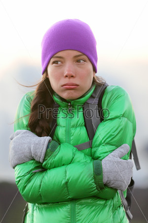 Freezing woman feeling cold outdoors trying to keep warm shaking and shivering wearing hat and gloves outside hiking on hike.