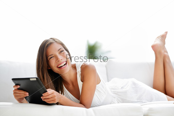 Tablet computer. Young woman laughing in sofa lying down. Lifestyle with young caucasian asian mixed race woman model smiling using tablet pc in sofa at home outdoor in summer smiling happy.