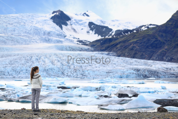 Adventure woman by glacier nature on Iceland. Tourist in Icelandic sweater by glacial lagoon / lake of Fjallsarlon, Vatna glacier, Vatnajokull National Park. Young woman visiting nature landscape.