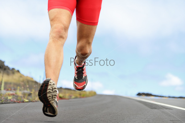 Running sport shoes and legs. Man runner legs and shoes in action on road outdoors at sunset. Male athlete model.