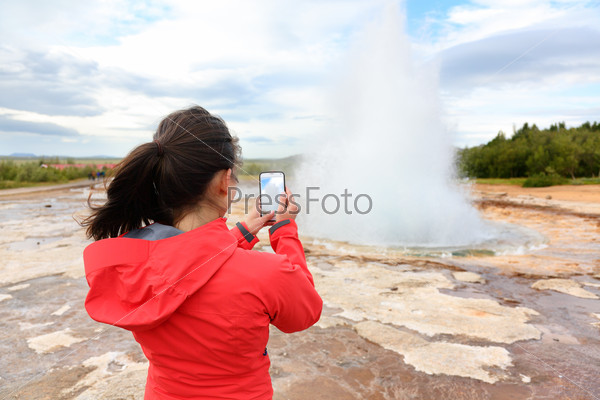 Iceland tourist taking photos of geyser Strokkur. Woman visiting famous tourist attractions and landmarks on the Golden Circle. Girl on holiday vacation sightseeing Icelandic nature.