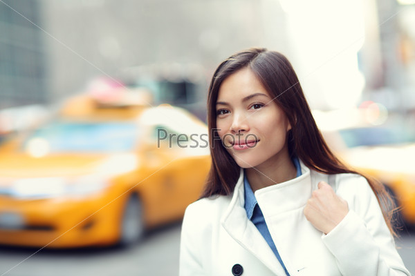 Young urban professional business woman in New York City Manhattan. Woman walking in street wearing coat downtown with yellow taxi cabs in background. Multiracial Asian Caucasian businesswoman in USA.
