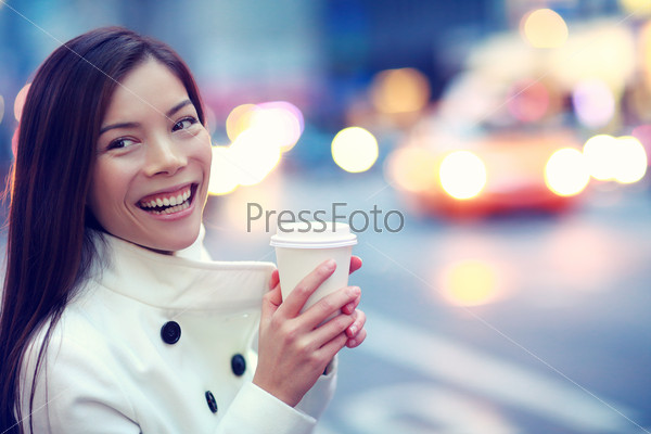 Professional young urban casual business woman happy in New York City Manhattan drinking coffee walking in street wearing coat downtown with yellow taxi cabs in background.