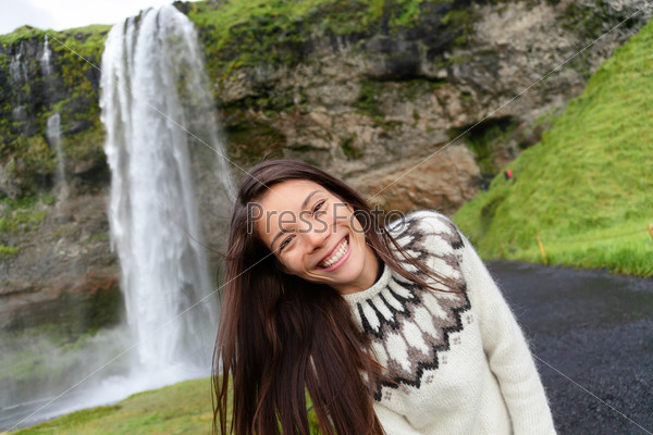 Woman on Iceland in Icelandic sweater by waterfall outdoor fun. Candid beautiful female model in nature landscape with tourist attraction Seljalandsfoss waterfall on Ring Road.