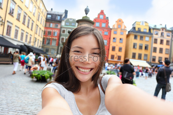 Asian woman taking self portrait selfie photo on Europe travel. Happy candid tourist on Stortorget, big square, Gamla Stan, the old town of Stockholm, Sweden.