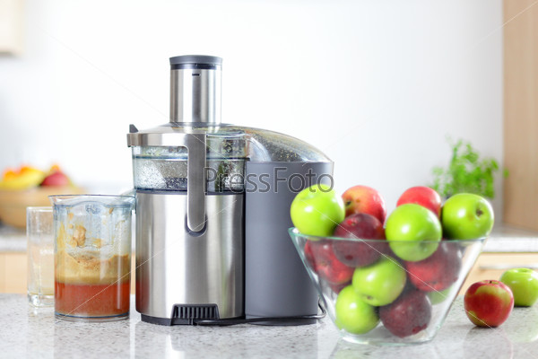 Apple juice on juicer machine - juicing concept. Apples in bowl in kitchen and fresh pressed juice.
