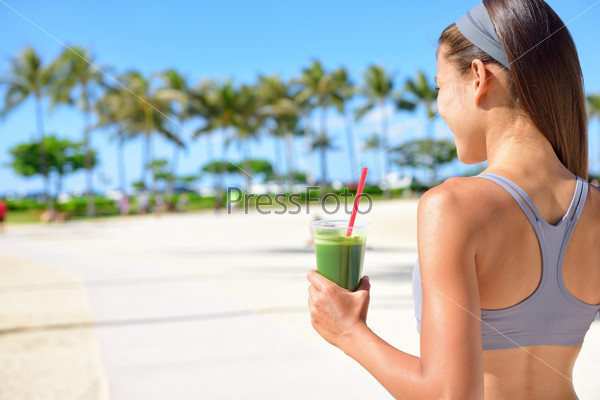 Woman drinking vegetable Green detox smoothie after fitness running workout on summer day. Fitness and healthy lifestyle concept with beautiful fit mixed race Asian Caucasian model outside on beach.