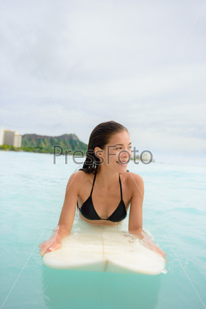 Surfing surfer girl looking for surf on surfboard. Female bikini woman living healthy active water sports lifestyle on Hawaiian beach. Asian Caucasian model on Waikiki Beach, Oahu, Hawaii.