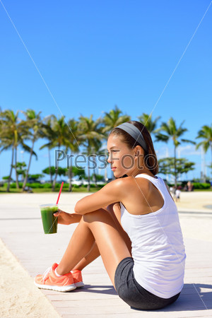 Exercise woman runner drinking green vegetable smoothie resting and relaxing after running.  Fitness and healthy lifestyle concept with multiracial Asian Caucasian female model.