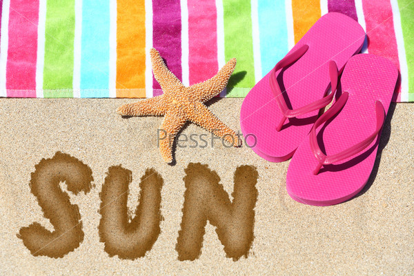 Word - Sun - on a tropical beach with a striped towel in the colors of the rainbow, pink slip slops and a sea star on sunny golden sand symbolic of travel and a summer vacation in the tropics