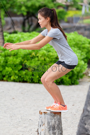 Fitness woman athlete bench jump squat jumping outside in nature landscape. Strength training fit girl working out exercising outdoors on beach in summer doing jumping on tree trunk.