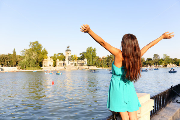 Happy success woman in Madrid park El Retiro. Successful girl cheerful with arms up outstretched in by lake Parque el Retiro in Madrid, Spain, Europe. Woman in summer dress.