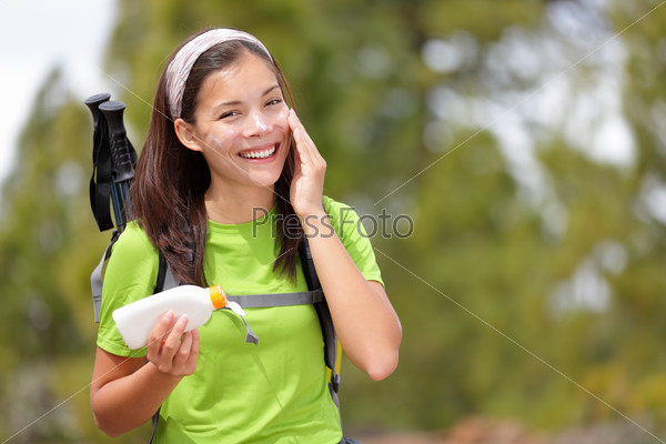 Hiker sunscreen. Woman hiking putting sun block lotion outdoors during summer hike holidays. Mixed race Caucasian Asian female model.