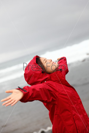 fall woman in rain happy by ocean. Woman enjoying rainy grey autumn day by the sea. Happy asian caucasian woman outdoor.