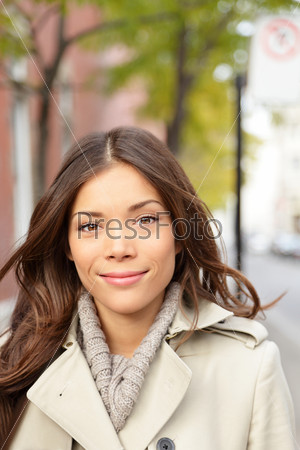 City woman portrait. Young beautiful multiracial woman walking in city wearing trench coat smiling at camera. Mixed race Asian Chinese / Caucasian female model.