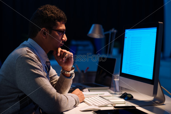 Young man working on computer at night in dark office