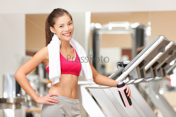 Fitness woman in gym. Portrait of fit workout girl with towel standing by treadmills in fitness club. Happy smiling young multicultural fitness model.