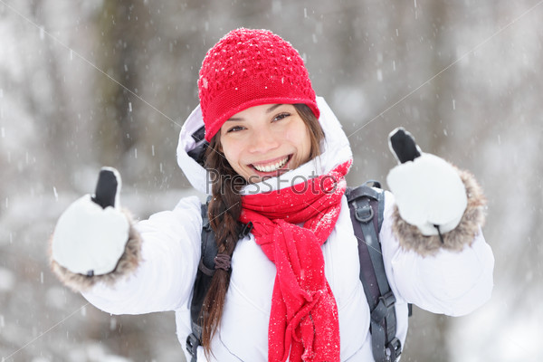 Happy young Asian woman with a beautiful vivacious smile dressed warmly in winter clothes standing outdoors in a snowstorm giving thumbs up gesture of approval