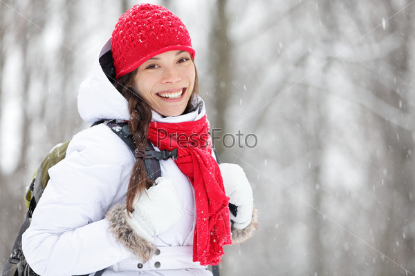 Woman winter hiking. Beautiful young Asian woman enjoying the falling snow dressed in a cheerful red winter scarf and cap and with a satchel on her back with copyspace.