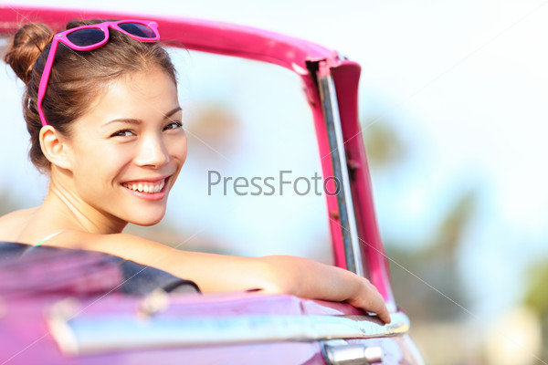 Car woman happy in old pink retro vintage car. Young woman driving on road trip on beautiful sunny summer day. Pretty mixed race Asian / Caucasian female model.