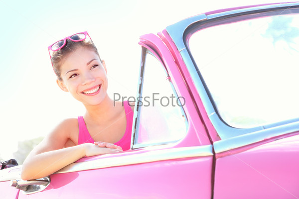 Woman driving vintage car. Retro style image of happy smiling young woman in old pink car going on road trip on sunny spring or summer day. Beautiful multiracial Caucasian / Asian in Havana, Cuba.