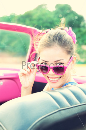 Vintage woman in pink retro car. Retro vintage processed photo of girl on road trip driving in vintage cabriolet car during summer holidays.