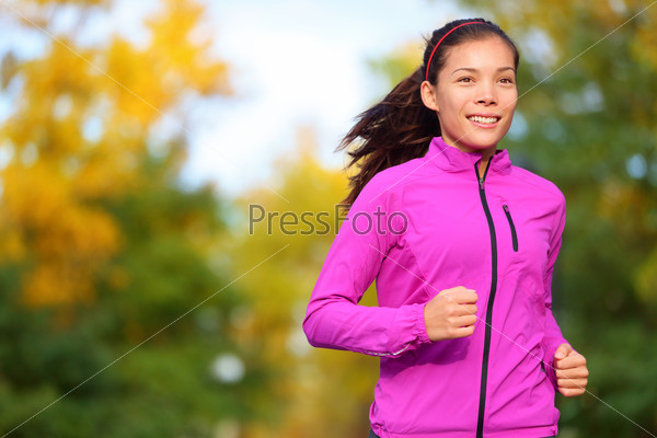 Running woman jogging in autumn forest in fall. Beautiful female runner wearing autumn running jacket. Healthy lifestyle photo with beautiful mixed race ethnic Chinese Asian and Caucasian fitness girl