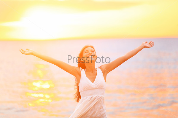 Freedom woman happy and free open arms on beach at sunny\
sunset. Beautiful joyful elated woman looking up smiling by the\
ocean during summer holidays vacation. Pretty multiracial Asian\
Caucasian girl.