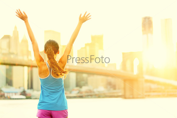 Happy cheering woman in New York City enjoying view and sun on Brooklyn Bridge. Fit female fitness runner joyful and excited after running.