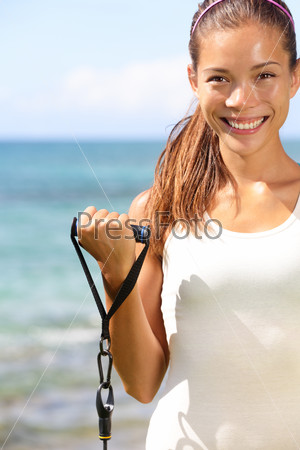 Fitness girl training at beach with elastics resistance bands. Fit sporty woman strength training biceps outdoors using elastic. Mixed race Asian Caucasian sport model outside working out.