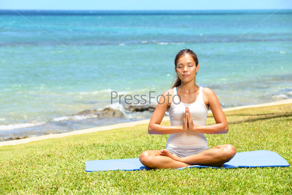 Yoga woman meditating woman relaxing by ocean sea doing the Sukhasana, easy pose. Woman in meditation in beautiful ocean landscape retreat. Meditation, yoga and relaxation concept.