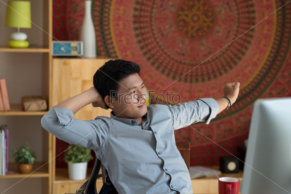 Smiling young man stretching while sitting at his workplace