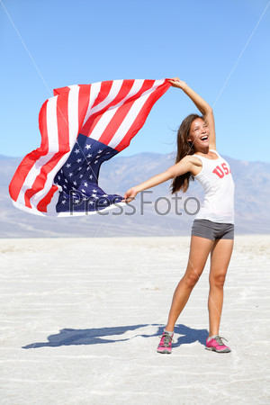 US flag - woman athlete showing american flag. USA sport athlete winner cheering waving stars and stripes outdoors in desert nature. Beautiful cheering happy young multicultural girl joyful excited.